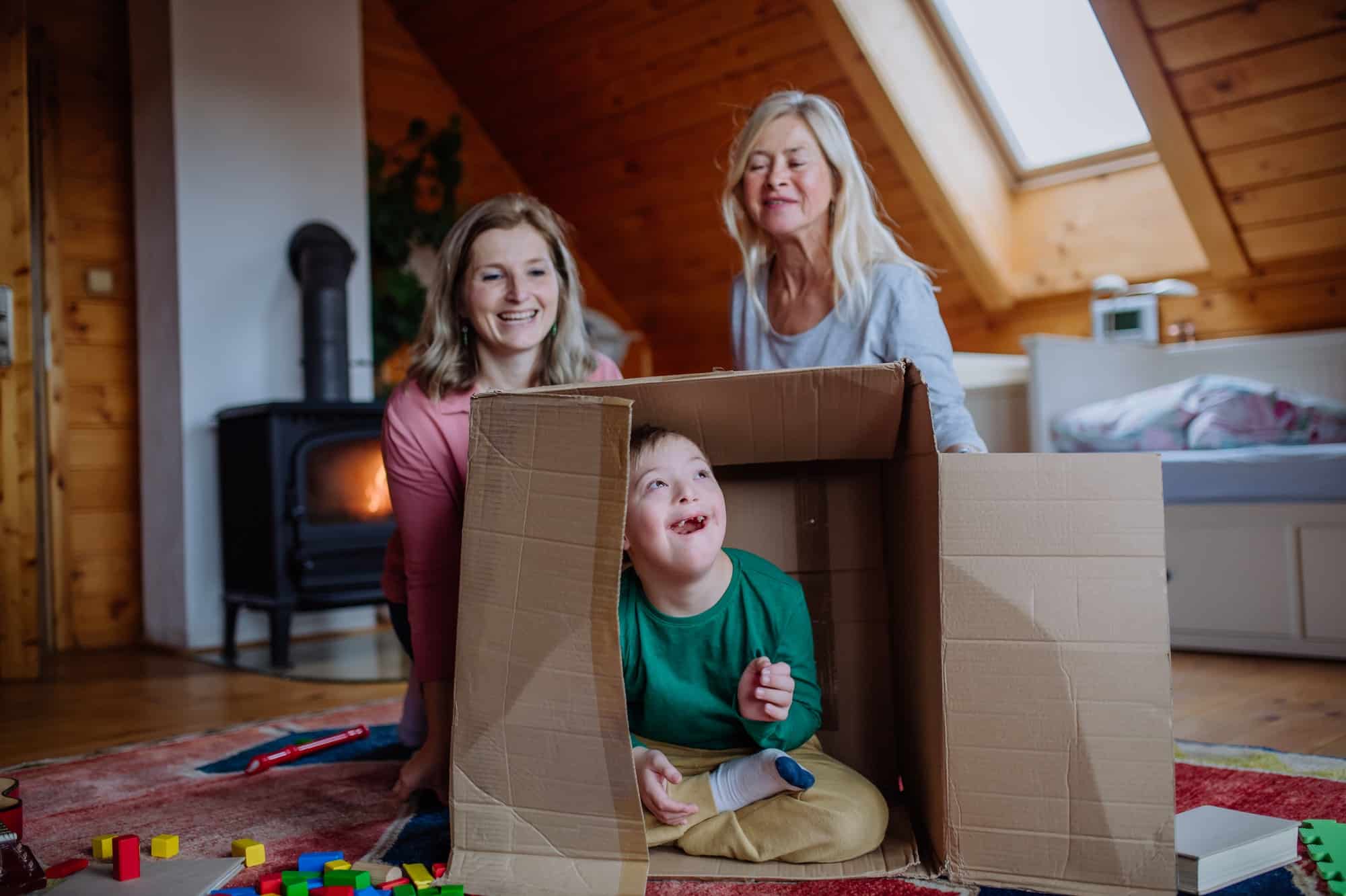 Boy with Down syndrome with his mother and grandmother playing with box together at home